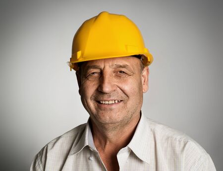 Close up portrait of happy smiling mature engineer or builder in yellow hardhat posing in studio.の写真素材