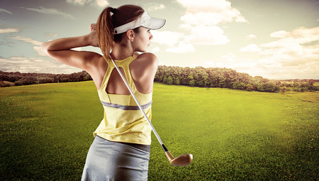 Young female in sportswear playing golf on green field. Active fresh Caucasian woman swinging with golf club.の写真素材