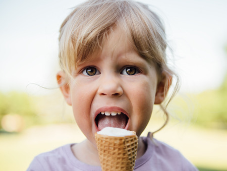 Cute baby girl eating ice cream in the park on weekend. Close-up portrait of pretty small Caucasian child with delicious dessert outdoors.の写真素材