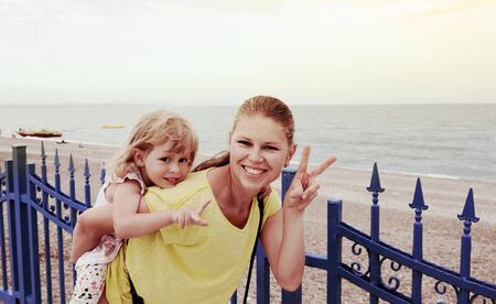 Young mother holding her daughter walking on bridge at seaside