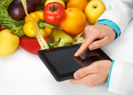 Close-up of female dietitian hands holding tablet pc in her office. Concept of diet, medicine and technology.の写真素材