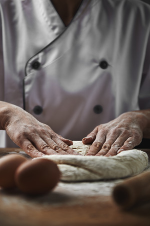 Professional baker making bread dough on wooden table with baking ingredients.の写真素材