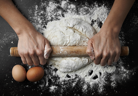 Close-up of female hands rolling dough with pin on wooden table. Concept of cooking and homemade...