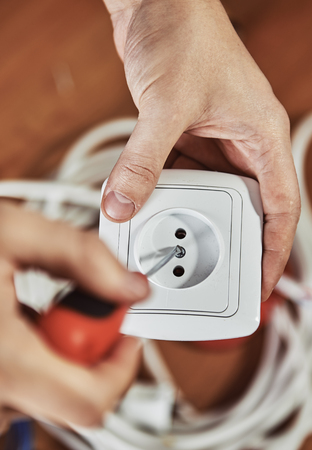 Close-up of electrician hands installing socket in a house over cables background. Male laborer working with screwdriver.の写真素材