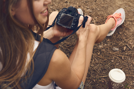 Female photographer holding dslr camera sitting on the ground in the forest. Concept of tourism,...