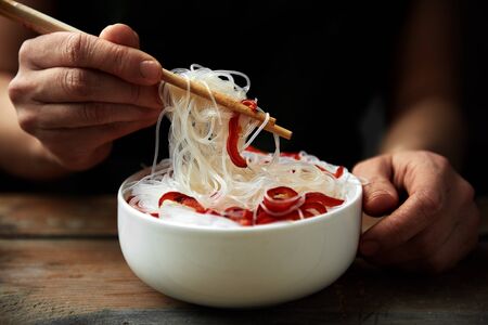 Closeup of cooked noodles with vegetables. Woman eating asian meal with chopsticks.の写真素材