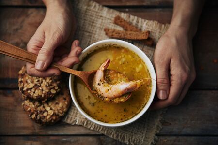 Close-up of human hands with wooden spoon eating seafood soup. Traditional asian cuisine.の写真素材