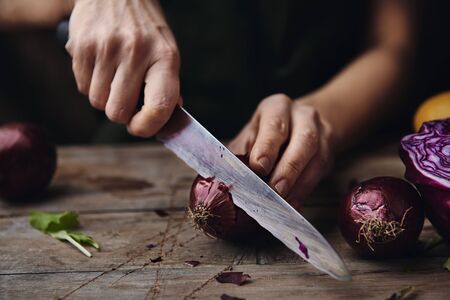 Female gardener cutting fresh onion at home in the kitchen.