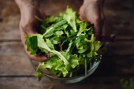 Healthy food concept. Woman chef mixing green fresh salad leaves in a bowl.