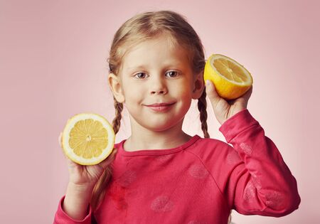 Cute girl with juicy lemon posing over pink background. Healthy childhood concept.の写真素材