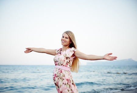 Portrait of happy pregnant woman with open arms standing on seashore at sunset.の写真素材