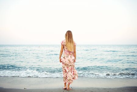 Young woman in summer dress looking at beautiful seascape at dawnの写真素材