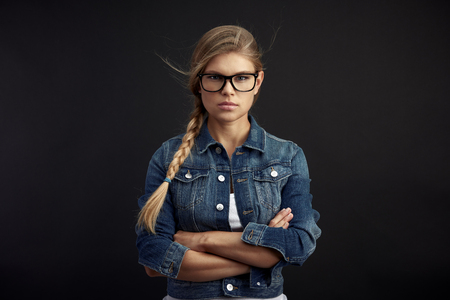 Serious female wearing stylish spectacles, posing in studio on black background.の写真素材
