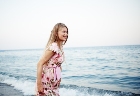 Pretty smiling female in floral dress running on seashore at sunset.の写真素材