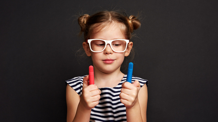 Portrait of thinking girl holding colorful pencils over black background.の写真素材