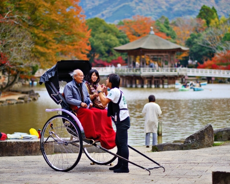NARA, JAPAN - NOVEMBER 18: A rickshaw runner enthusiastically explains the ride to tourists November 18, 2012 in Nara, JP. Rickshaws are commonly believed to have been invented in Japan in the 1860s.のeditorial素材