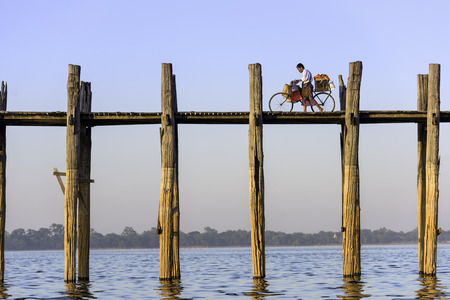 MANDALAY, MYANMAR - OCTOBER 26, 2015: A cyclist pushes his bike across the U Bein Bridge over Taungthaman Lake. The bridge was built around 1850 and is the oldest and longest teakwood bridge in the world.のeditorial素材
