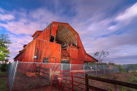 An old red barn in ruins in a rural setting at twilight.の写真素材