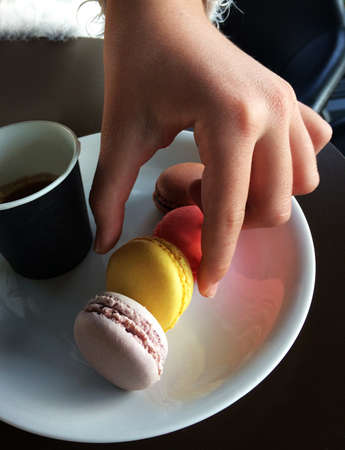 hand picking a macaron, french colorful round pastry, in a plate with a coffe cupの写真素材