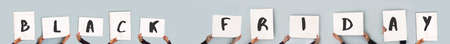 Black Friday written on eleven white blank rectangular signs hold by women's hands, panoramic banner with seven white blank signs on a clear blue nackgroundの写真素材