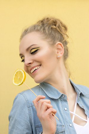 A nice girl with bright makeup tilted her head and laughs. She holds a lemon in her handの写真素材