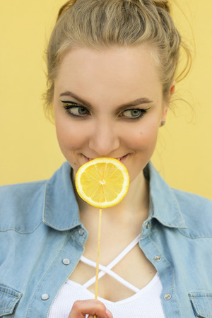 beautiful girl with bright yellow makeup. Holds the lemon as a lollipop.の写真素材