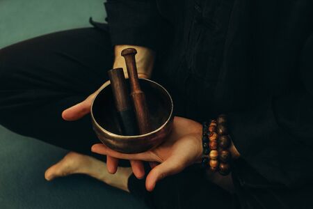 Top view of two hands of a man holding a singing bowl with sticks in front of him. Listen to the...