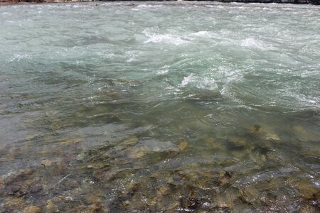 Cold water flows with white splashes in a mountain stream rapids in the North Cascades