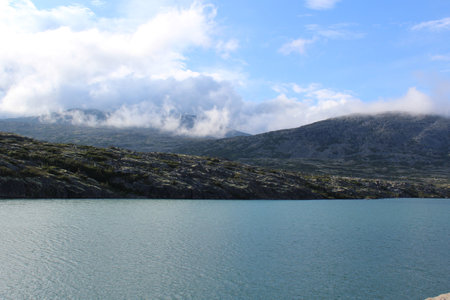 Clouds hanging over the top of mountains and an alpine lake in the Alaskan wildernessの写真素材