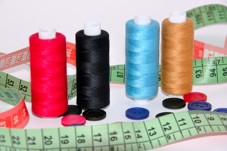 Multi-colored threads, buttons and measuring tape on a white background