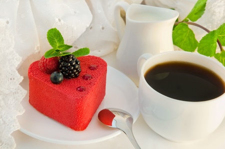 Cake in the form of heart with a blackberry, a raspberry and mint, a cup of coffeeの写真素材