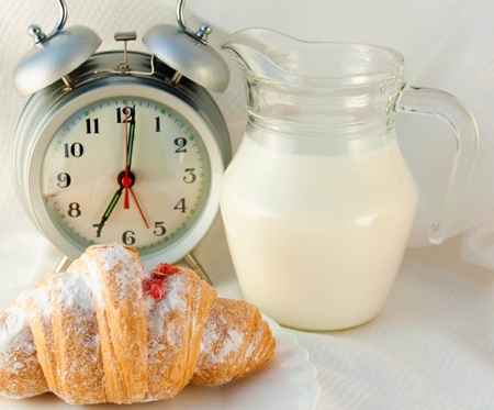 Croissant with jam and a jug of milk and an alarm clock, a light morning mealの写真素材