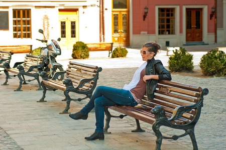 The beautiful young girl sits on a bench in the old city