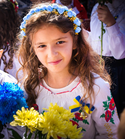 Ukrainian Schoolgirl in a wreath and embroidered shirt and with patriotic flowers against the war in...