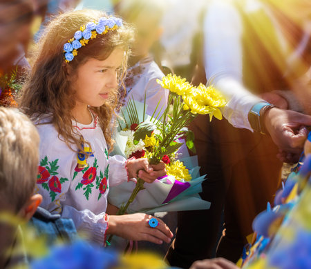 Ukrainian Schoolgirl in a wreath and embroidered shirt and with patriotic flowers against the war in...
