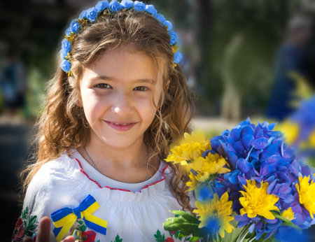 Ukrainian Schoolgirl in a wreath and embroidered shirt and with patriotic flowers against the war in Ukraineの写真素材