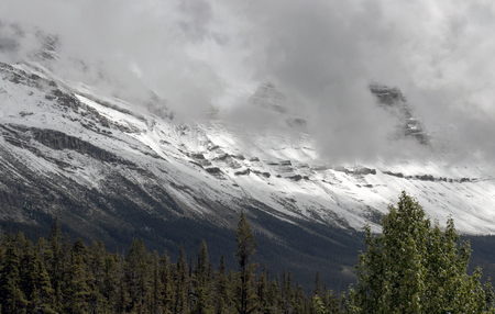 A massive mountain range covered in snow and obscured by clouds in Banff National Park in Alberta, Canada.の写真素材