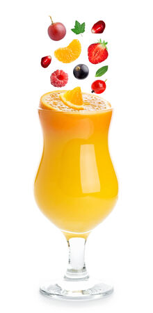 Fruits and berries fall in a glass of orange juiceの写真素材