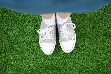 White sneakers on girl legs on green grassの写真素材