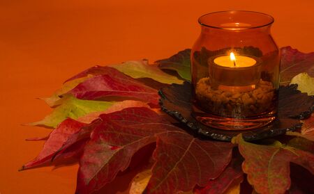 Candle in a glass on colorful autumn leavesの写真素材