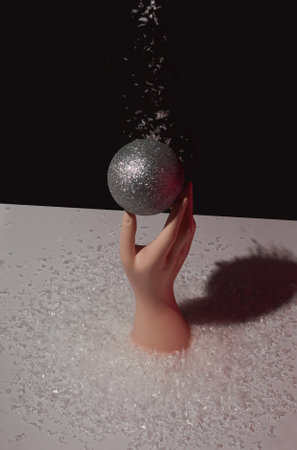 Hand holds a Christmas ball on which snow is falling. Minimal New Year concept. Winter holidays background.の写真素材