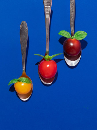 Cherry tomatoes with basil in spoons on a blue background. Minimal creative food concept. Flat lay, top viewの写真素材