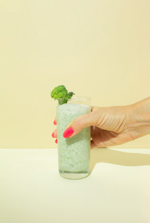 Woman's hand hold a broccoli smoothie in a glass. Minimal healthy composition.の写真素材