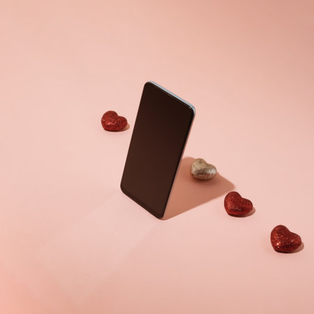 Smartphone screen standing in front of a row of sparkling red hearts on a pastel pink background. Mobile app and online dating concept.の写真素材