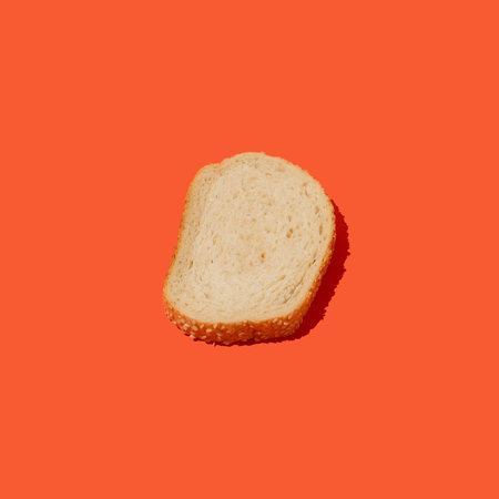 Overhead view of arranged slice of fresh white bread with sesame seeds against orange background. Bakery conceptの写真素材