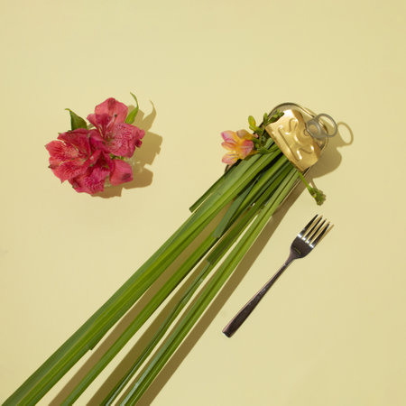 Still life of gold tin can full of fresh grass and pink flower, with fork on pastel background. Top...
