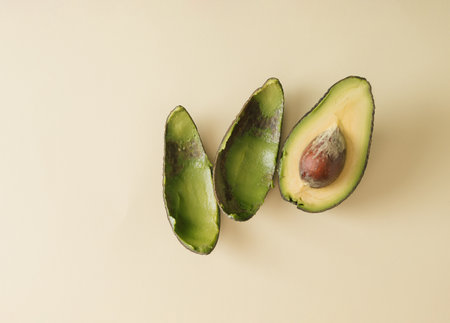 Emptied shell of an avocado and half avocado with copy space on beige background. Sliced fresh...