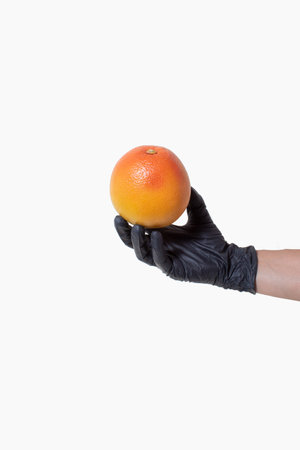 Hand with a black glove holds a grapefruit on bright background. Creative concept of clean healthy foodの写真素材
