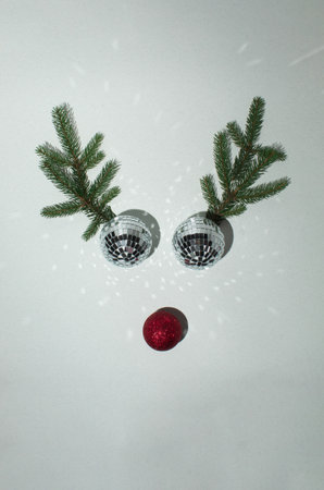 Christmas disco balls bauble with reindeer antlers made of evergreen branches on white background. Minimal New year concept. Flat lay.の写真素材