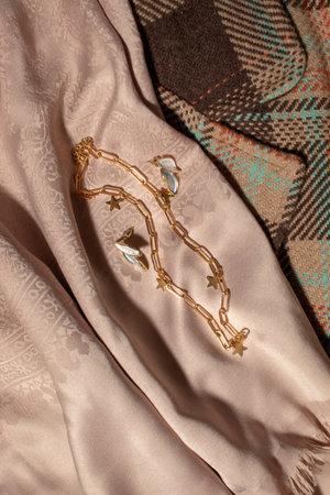 A gold necklace and earrings on a mocha scarf next to a brown coat. Creative fashion ideaの写真素材